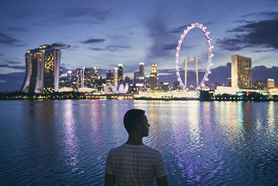 Rear view of man standing against illuminated ferris wheel by river