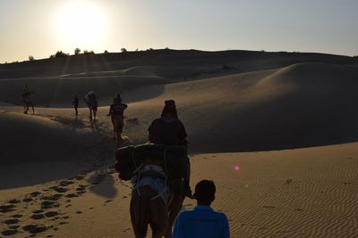 Rear view of people walking on sand at beach