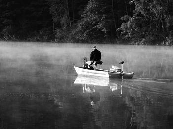 Rear view of man sitting on fishing boat at lake