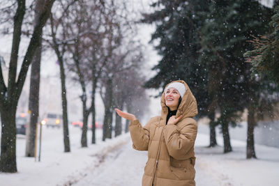 A happy woman walks through the city in winter and catches snow with her hand