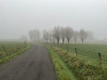 Road amidst field against sky during foggy weather