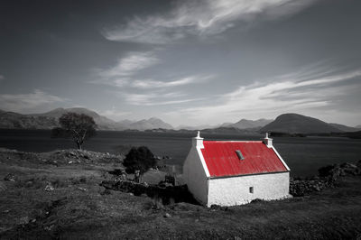 View of lone house on riverbank against cloudy sky