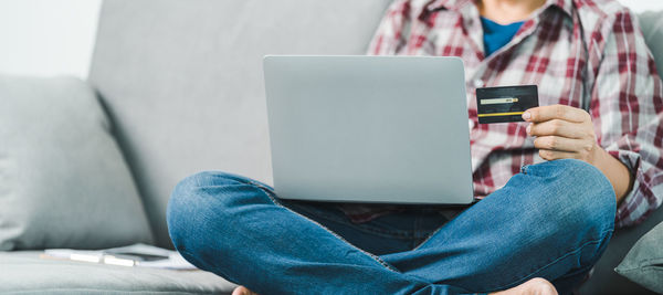 Midsection of man using mobile phone while sitting on sofa