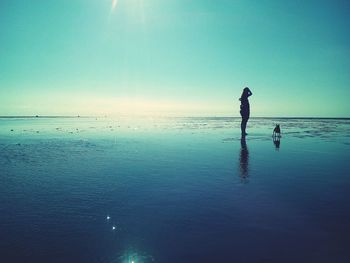 Woman with dog standing at beach against sky