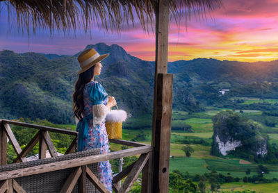 Woman looking away while standing by railing against sky