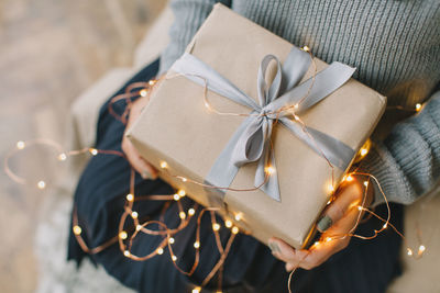 Midsection of woman holding christmas present with illuminated string lights