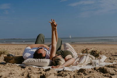 Rear view of woman sitting on sand at beach against sky