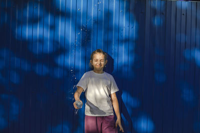 Sunny splashes, teenage girl radiates joy against a vivid blue wall