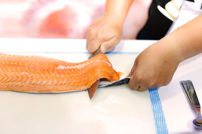 Cropped hands of chef cutting fish in commercial kitchen