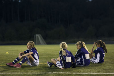 Athletes relaxing on soccer field against trees