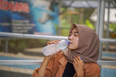 Asian muslim woman wearing a beautiful hijab is drinking bottled water