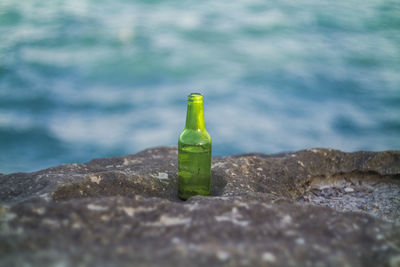 Close-up of rocks and a green glass bottle by sea 