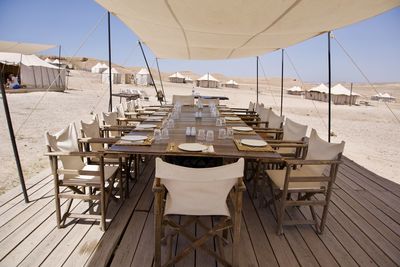 Empty chairs and tables at restaurant by sea against sky