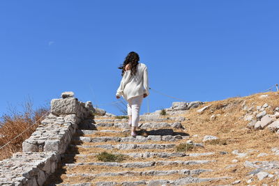 Woman walking on staircase against clear blue sky