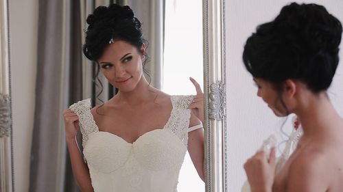 Reflection of bride trying wedding dress in fitting room on mirror