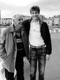 Happy grandfather and grandson standing against sky in city