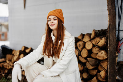 Smiling young woman sitting against firewood