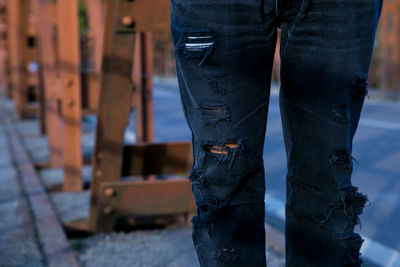 Midsection of person in torn jeans while standing by road