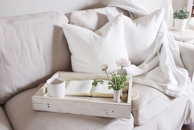 High angle view of coffee with book and flower vase on sofa at home