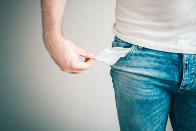 Cropped image of man pulling empty pocket against gray background