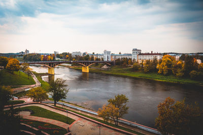 Bridge over river by cityscape against sky