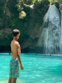 Shirtless man looking at waterfall