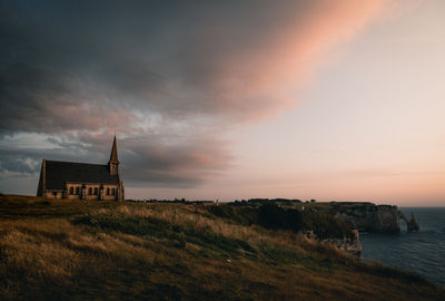 Built structure on land by sea against sky during sunset