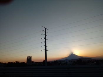 Silhouette electricity pylons against clear sky during sunset