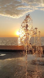 Close-up of sea waves splashing on beach against sky during sunset