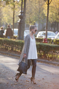 Portrait of young woman standing on footpath in park