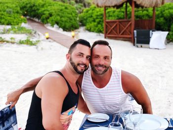 Portrait of smiling men with arm around sitting at beach