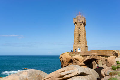 Low angle view of lighthouse by building against blue sky