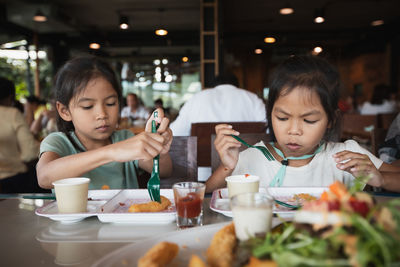 Cute sisters eating food while sitting at restaurant