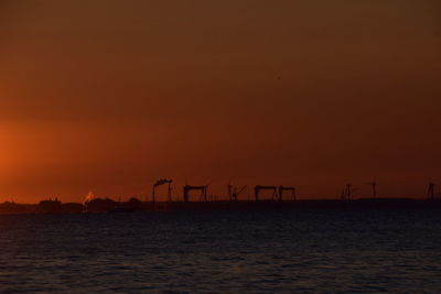 Silhouette cranes against sky during sunset