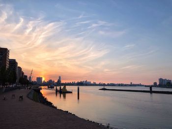 Scenic view of river by buildings against sky during sunset