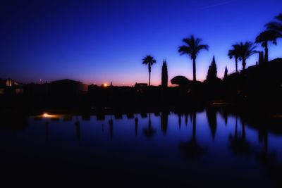 Silhouette palm trees by lake against sky during sunset