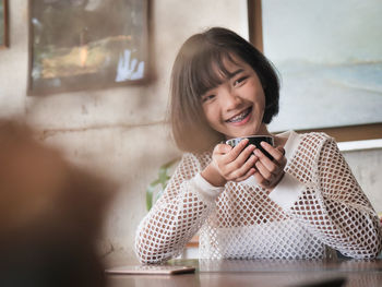 Smiling teenage girl holding coffee cup while sitting in cafe