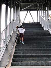 A boy climbs up a stair while pushing his bicycle