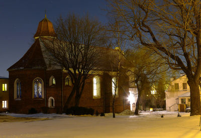 Illuminated building by trees against sky