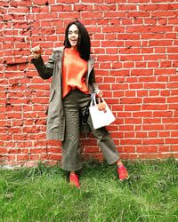 Portrait of young woman standing against red brick wall