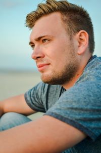 Portrait of young man looking away while sitting on beach