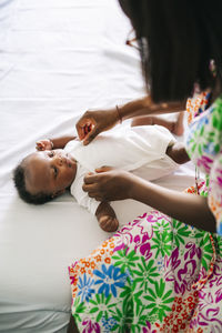 Mother adjusting bib for baby lying on bed at home