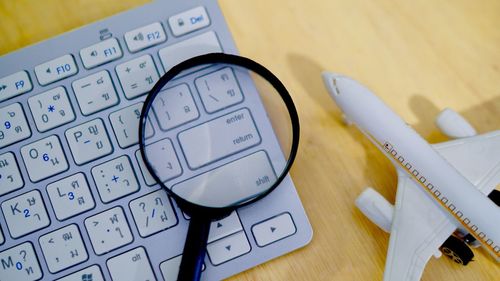 High angle view of magnifying glass on keyboard by toy airplane at table