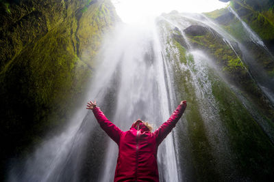 Midsection of woman standing by waterfall in forest