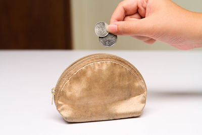 Cropped hand putting coins in purse on table