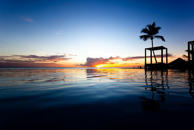 Silhouette swimming pool by sea against sky during sunset