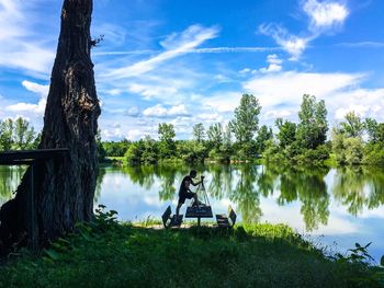 Man sitting by lake against sky