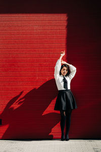 Full length portrait of woman standing against red wall