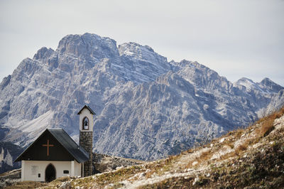 Spectacular scenery of small church with bell tower against rough mountain ridge at daytime