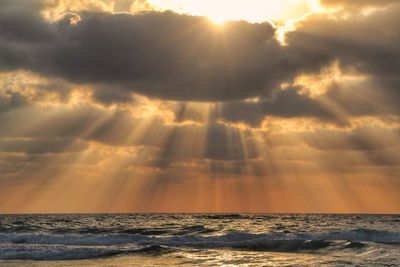 Sunlight streaming through clouds over sea during sunset